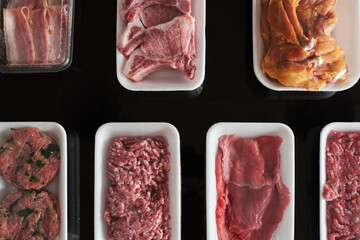 Raw meat in trays on black background