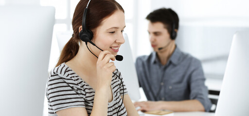 Casual dressed young woman using headset and computer while talking with customers online. Group of operators at work. Call center, business concept