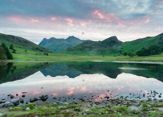 On a calm summer morning the flat Blea tarn reflects the Langdale Pikes as they wait for the sun to...