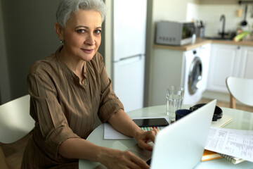Smiling middle-aged businesswoman working at home. Workplace at home. Distance working and remote work concept. Kitchen interior on blurred background