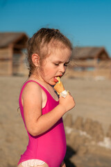 Cute little girl in a pink swimsuit with ice cream in a cone in hand on the sandy beach by the sea
