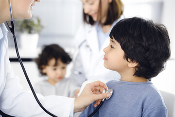 Doctor-woman examining a child patient by stethoscope. Cute arab boy at physician appointment. Medicine concept