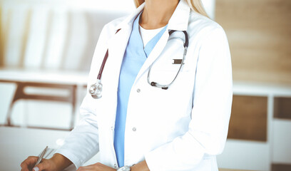 Unknown woman-doctor at work in sunny clinic. Female physician controls medication history record, close-up. Medicine concept