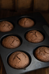 Homemade chocolate cupcakes in a cooking mold, standing on a wooden table.