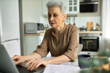 Serious middle-aged woman sitting at home workplace. Pensive and concentrated female making annual...