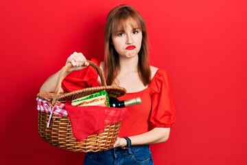 Redhead young woman holding picnic wicker basket with bread depressed and worry for distress,...