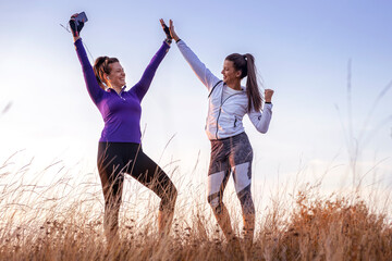 Obraz na płótnie Canvas Young and happy best female friends in sportswear making high five together after successful training in nature