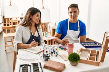 Two students smiling happy painting sitting on the table at art school.