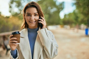 Young hispanic woman talking on the smartphone and drinking coffee at the park.