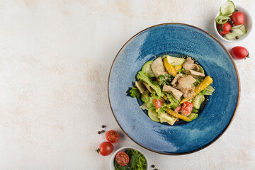 Salad with squid. Lettuce, zucchini, mini corn, tomatoes, squid and sauce on a blue plate on a light background.