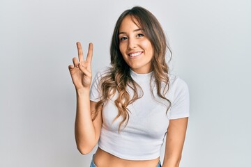 Fototapeta na wymiar Young brunette woman wearing casual white t shirt smiling looking to the camera showing fingers doing victory sign. number two.