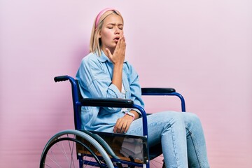 Beautiful blonde woman sitting on wheelchair bored yawning tired covering mouth with hand. restless...