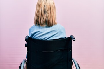 Beautiful blonde woman sitting on wheelchair standing backwards looking away with crossed arms