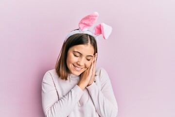 Young beautiful woman wearing cute easter bunny ears sleeping tired dreaming and posing with hands together while smiling with closed eyes.