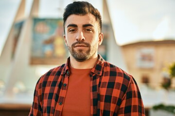 Young hispanic man with serious expression standing at the city.