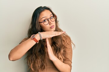Young hispanic girl wearing casual clothes and glasses doing time out gesture with hands,...