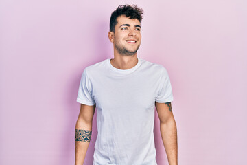 Young hispanic man wearing casual white t shirt looking to side, relax profile pose with natural face and confident smile.