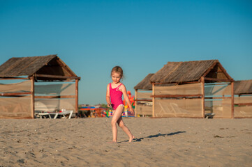 Adorable little girl in a pink leotard is engaged in gymnastics on a sandy beach - Powered by Adobe