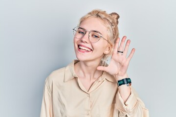 Beautiful caucasian woman with blond hair wearing casual look and glasses smiling with hand over ear listening an hearing to rumor or gossip. deafness concept.