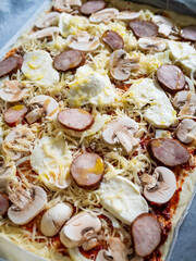 Pizza with white mushrooms, sausage, tomatoes, black olives, parmesan and mozzarella on wooden background

