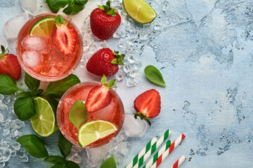 Two glasses of punch and fresh ingredients for making lemonade, infused detox water or cocktail. Strawberries, lime, mint, basil, ice cubes and shaker on grey stone or concrete background. Top view.