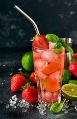 Glass of punch and fresh ingredients for making lemonade, infused detox water or cocktail. Strawberries, lime, mint, basil, ice cubes and shaker on black stone or concrete background. Selective focus