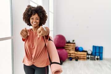 Fototapeta na wymiar African american woman with afro hair holding yoga mat at pilates room pointing to you and the camera with fingers, smiling positive and cheerful