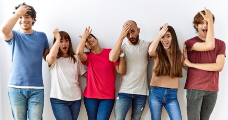 Obraz premium Group of young friends standing together over isolated background surprised with hand on head for mistake, remember error. forgot, bad memory concept.