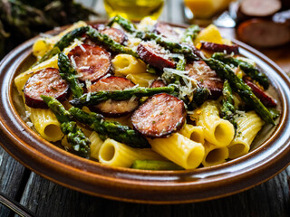 Tortiglioni with sausages, parmesan and asparagus on wooden table
