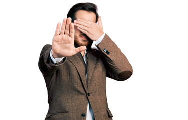 Young hispanic man wearing business jacket and glasses covering eyes with hands and doing stop gesture with sad and fear expression. embarrassed and negative concept.
