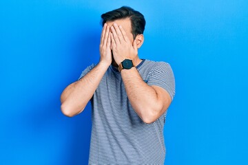 Handsome caucasian man with beard wearing casual striped t shirt with sad expression covering face with hands while crying. depression concept.