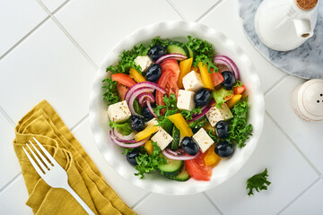 Traditional Greek salad of fresh cucumber, tomato, sweet pepper, lettuce, red onion, feta cheese and olives with olive oil on white plate. Healthy food, top view.