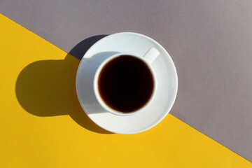 White cup with black coffee stands on the border of yellow and gray flowers