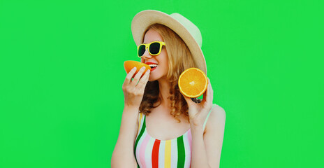 Summer portrait of happy smiling young woman eating slices of orange wearing a straw hat, sunglasses on green background