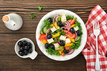 Traditional Greek salad of fresh cucumber, tomato, sweet pepper, lettuce, red onion, feta cheese and olives with olive oil on white plate. Healthy food, top view.