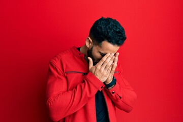 Young hispanic man wearing red leather jacket with sad expression covering face with hands while crying. depression concept.