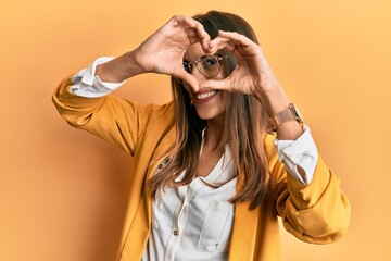 Young beautiful woman wearing business style and glasses doing heart shape with hand and fingers...