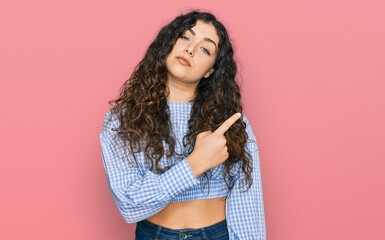 Young hispanic girl wearing casual clothes pointing with hand finger to the side showing advertisement, serious and calm face