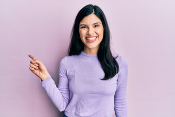 Young hispanic woman wearing casual clothes with a big smile on face, pointing with hand finger to the side looking at the camera.