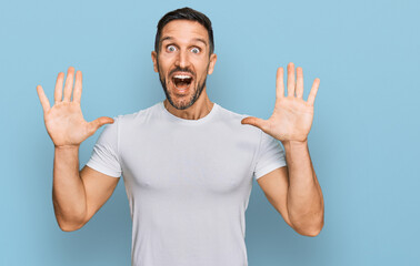 Fototapeta premium Handsome man with beard wearing casual white t shirt celebrating crazy and amazed for success with arms raised and open eyes screaming excited. winner concept