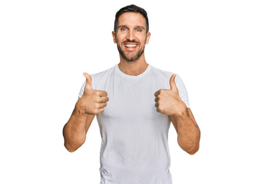 Handsome man with beard wearing casual white t shirt success sign doing positive gesture with hand, thumbs up smiling and happy. cheerful expression and winner gesture.
