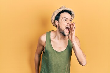 Young hispanic man wearing summer hat shouting and screaming loud to side with hand on mouth....