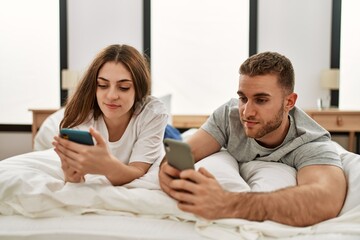 Young caucasian couple using smartphone lying on bed at home.