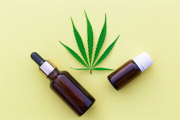 Bottle with pipette with hemp oil, cannabis leaf and seeds on yellow background