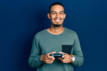 Young african american man playing video game holding controller smiling with a happy and cool smile on face. showing teeth.