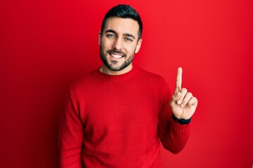 Young hispanic man wearing casual clothes smiling with an idea or question pointing finger up with...