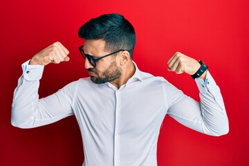 Young hispanic businessman wearing shirt and glasses showing arms muscles smiling proud. fitness concept.