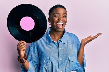 Young african american woman holding vinyl disc celebrating achievement with happy smile and winner expression with raised hand