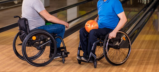 Two young disabled men in wheelchairs playing bowling in the club
