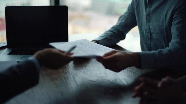 Close-up hands of unrecognizable two businesspeople signing agreement sitting at table with documents and laptop. Happy young couple taking financial advice signing paper document.